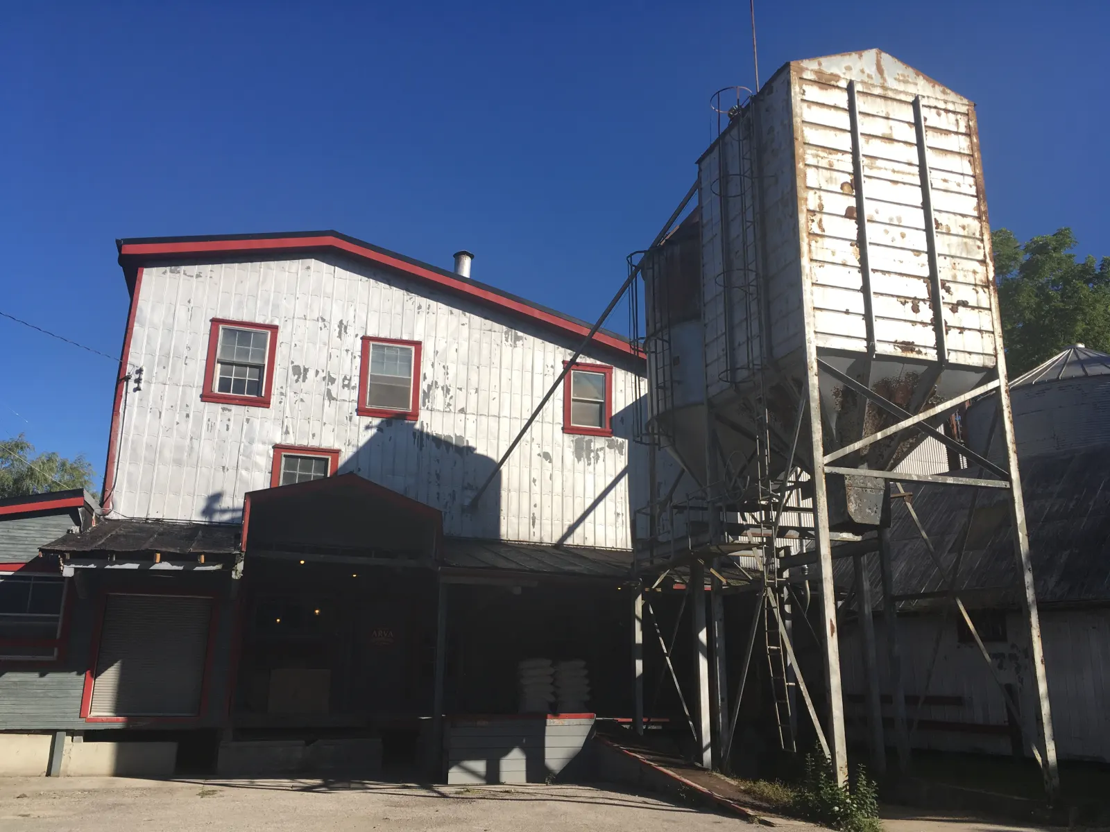 The Arva Flour Mills, a white wooden mill with red trim and a tall grain bin, under a blue sky