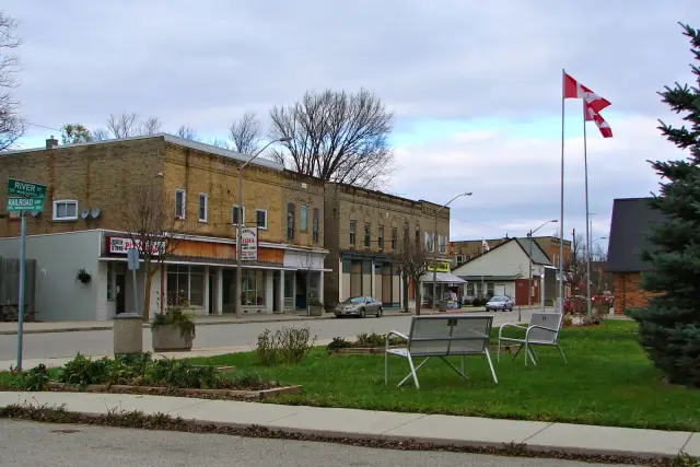 Alvinston's main street, a row of brick storefronts behind a small green with benches and flags