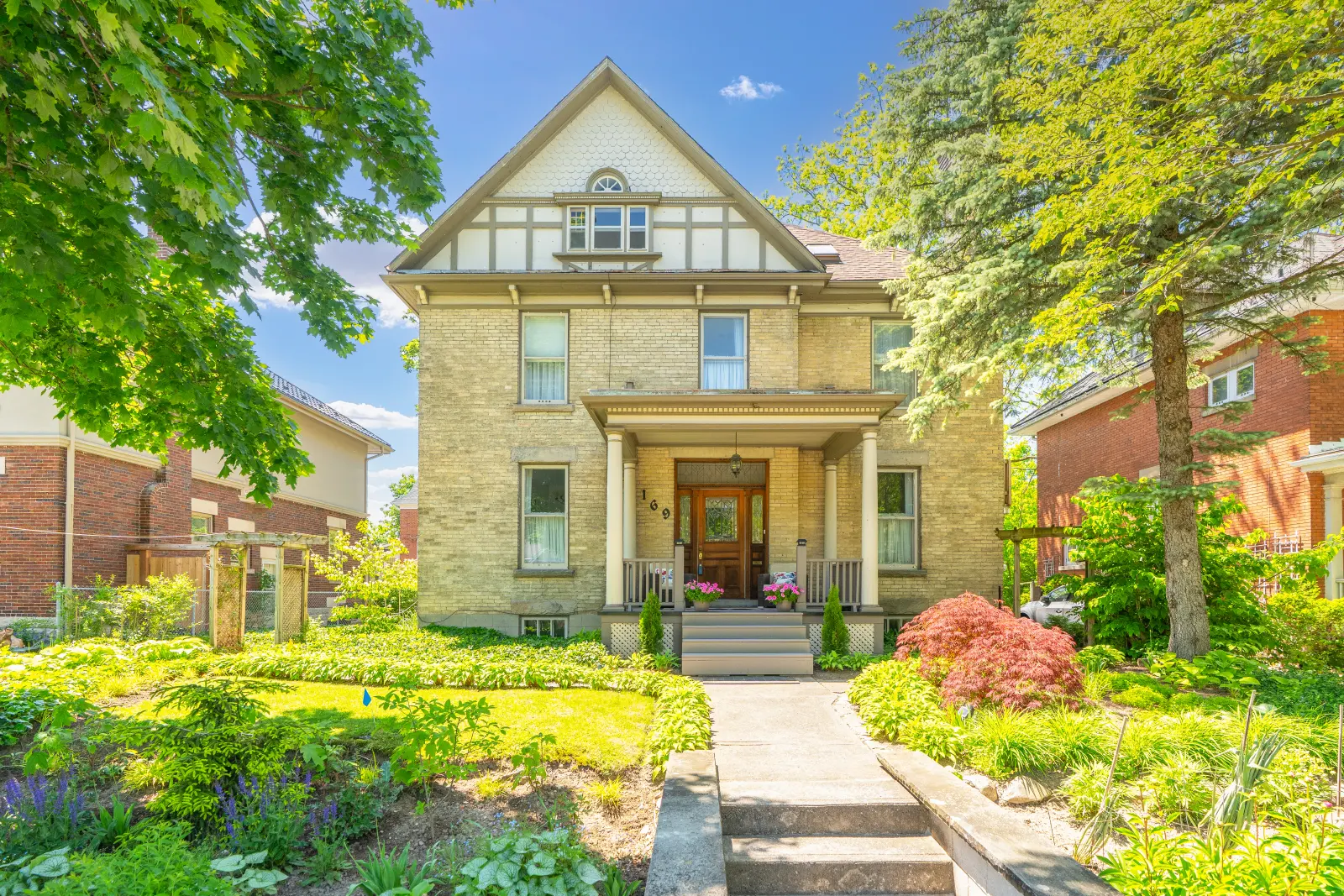 Front of the home: yellow brick, a half-timber gable and a covered porch behind summer gardens