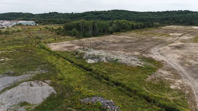 Open land with a grassy strip and wooded hills behind