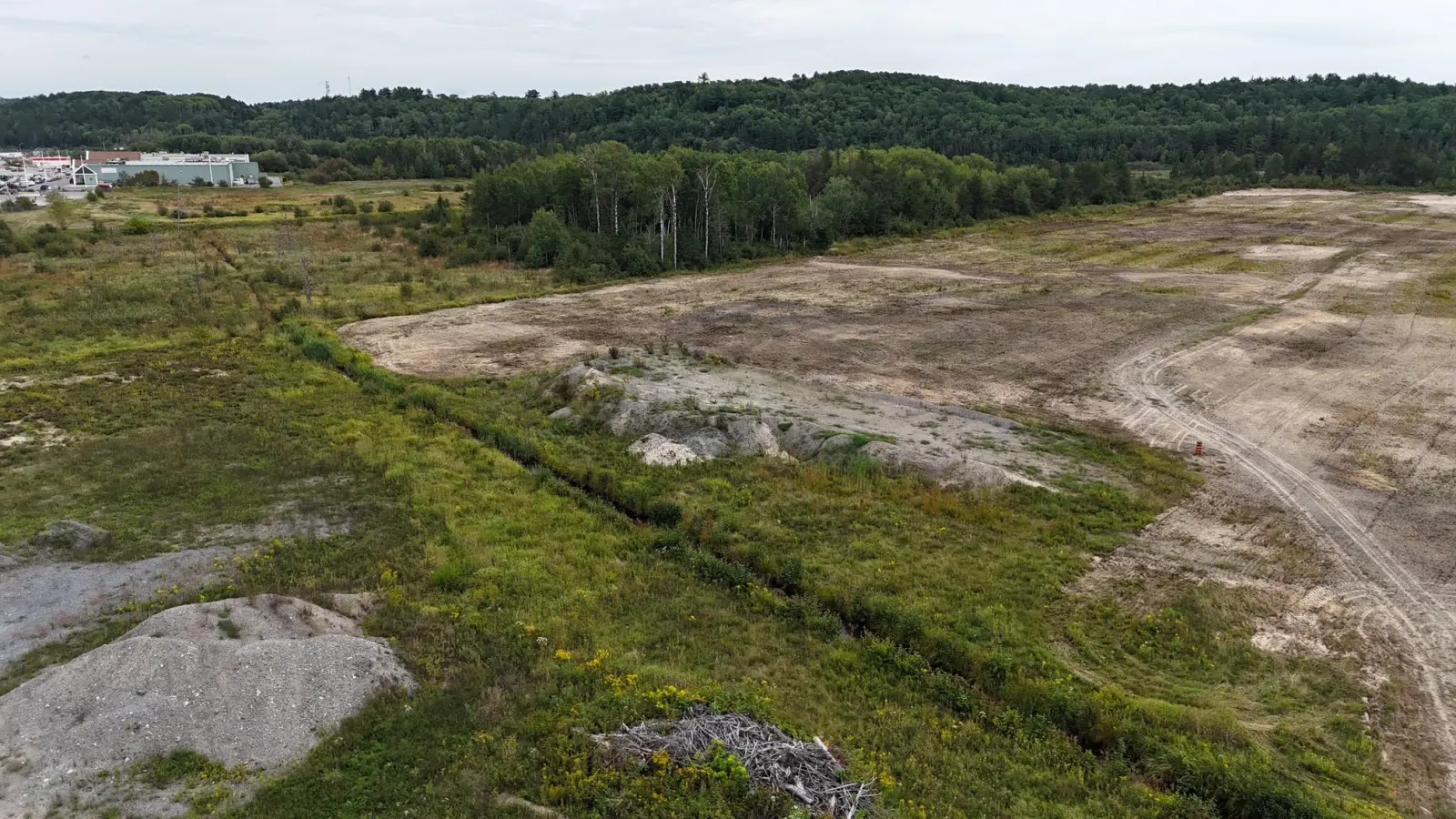 Open land with a grassy strip and wooded hills behind