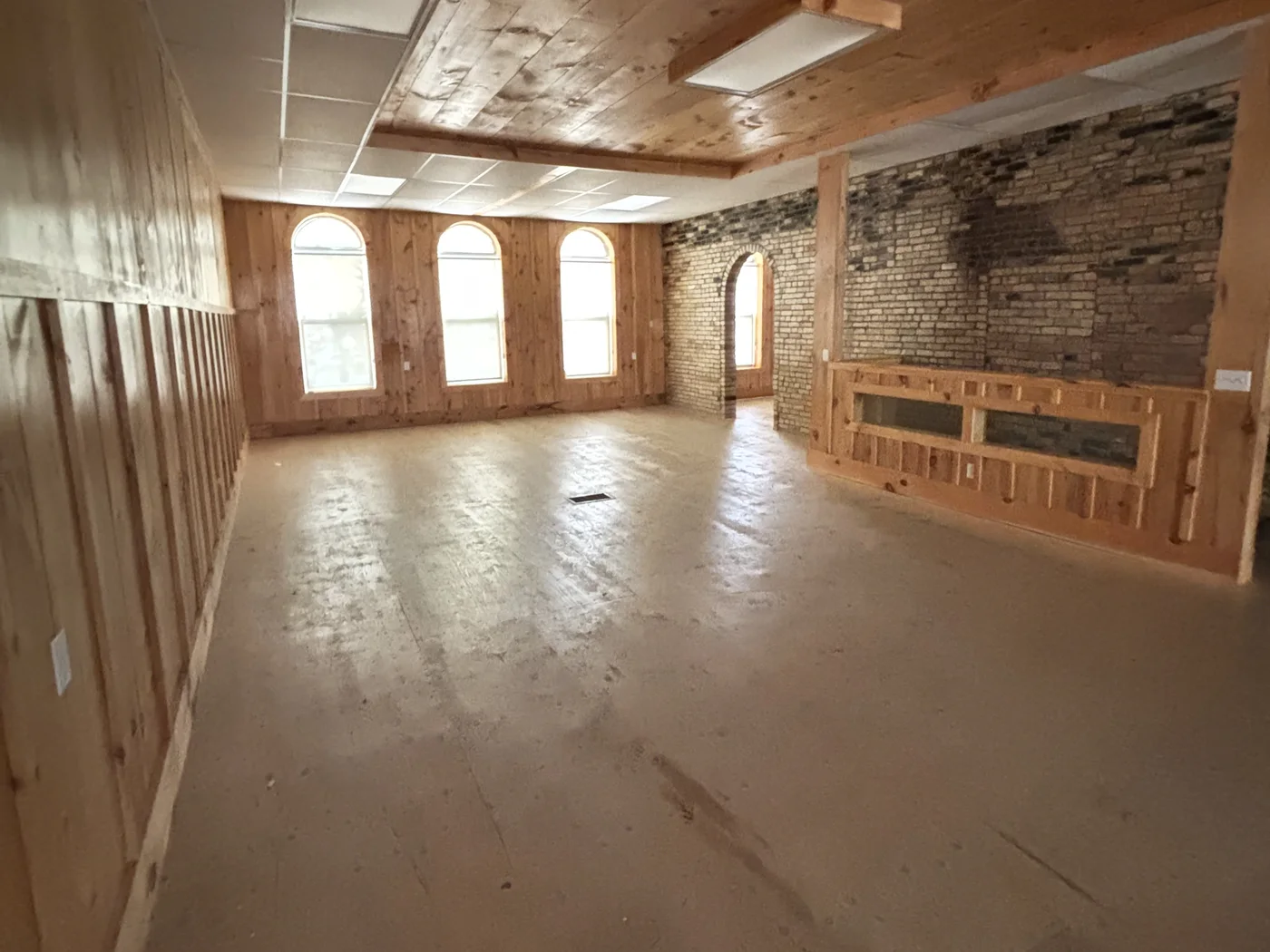 The second floor today: three arched windows, pine walls, an old brick wall with an arched doorway, a bare floor